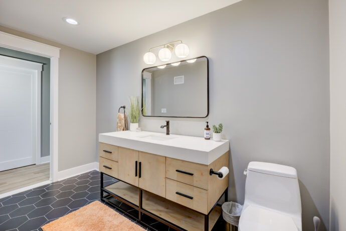 Modern bathroom vanity featuring custom white oak cabinetry, integrated white solid surface countertop, matte black faucet, black hexagon tile flooring, and a black-framed mirror.