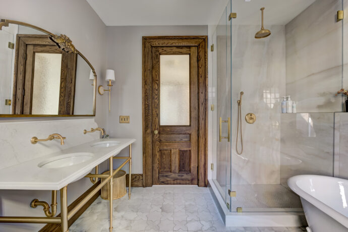 Historic Birmingham bathroom featuring a custom double vanity with Watermark Brooklyn unlacquered brass faucets, carved Anthropologie mirror, frameless glass shower, restored oak door, and TileBar Star & Cross porcelain flooring.