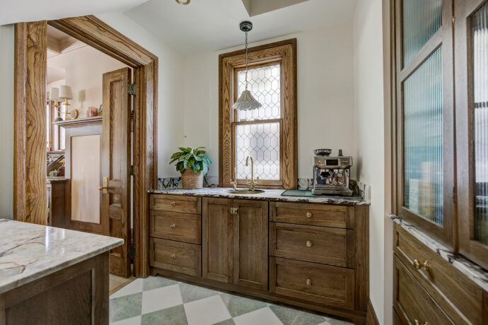 Custom butler's pantry in Birmingham, Michigan featuring Dura Supreme inset stained oak cabinetry, green and white checkered marble flooring, marble countertops, fluted glass cabinet doors, and an unlacquered brass sink and faucet.