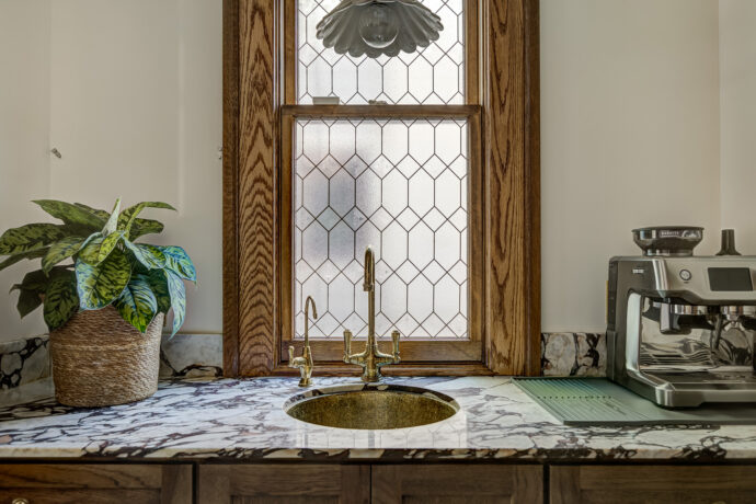 Custom coffee bar and butler's pantry with stained wood inset cabinetry, marble countertops, green and white marble checkerboard floor, brass hardware, and fluted glass cabinet doors.