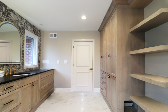 Custom white oak bathroom cabinetry with integrated storage, floating shelves, black quartz countertop, brass plumbing fixtures, and porcelain tile flooring in a luxury primary bathroom remodel.