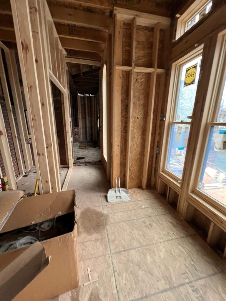 Newly framed hallway inside a first-floor addition, looking back through a doorway into the original 1906 house.
