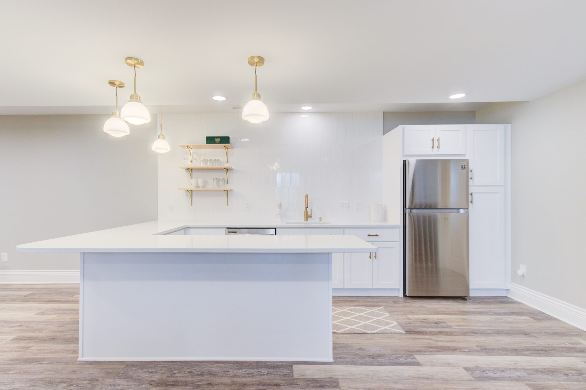 Basement kitchenette with a quartz island, white picket tile backsplash and full size refrigerator in Birmingham MI