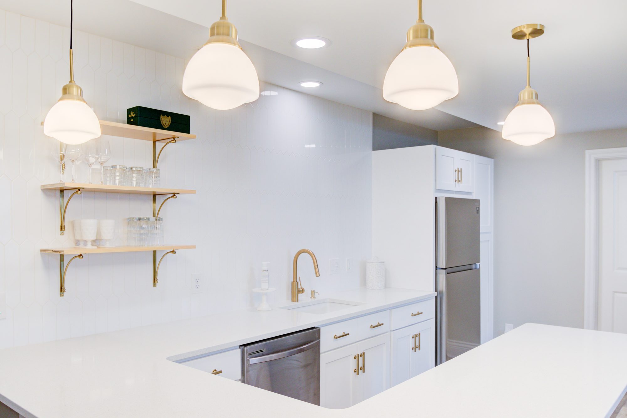 Schoolhouse pendants above the bar with brass bracket shelves against white picket tile in a Birmingham MI basement