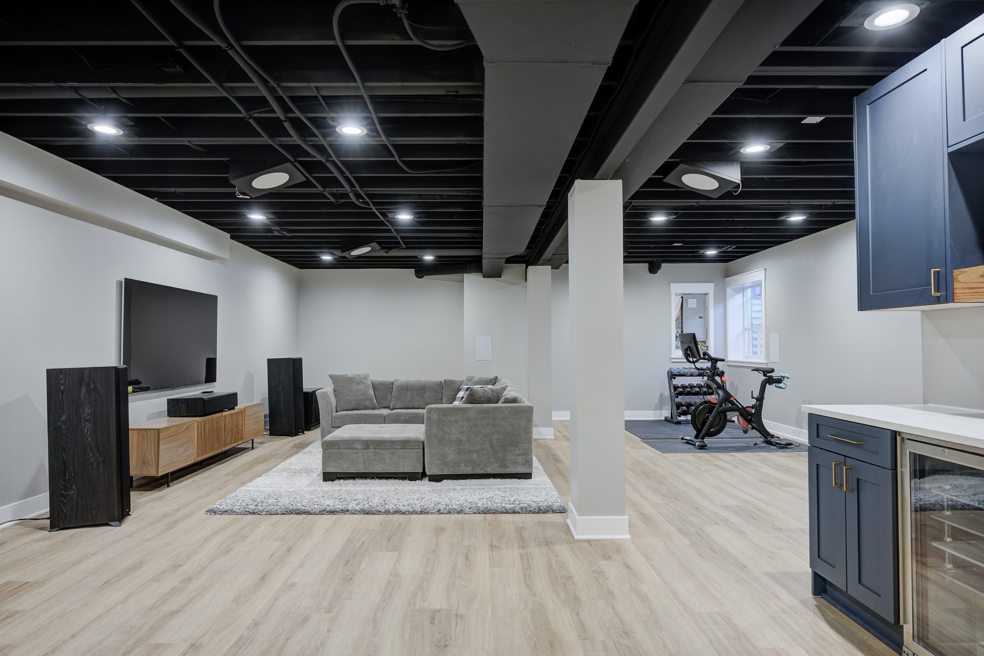 Finished basement in Royal Oak MI with a lounge, home gym and wet bar under a black painted exposed ceiling