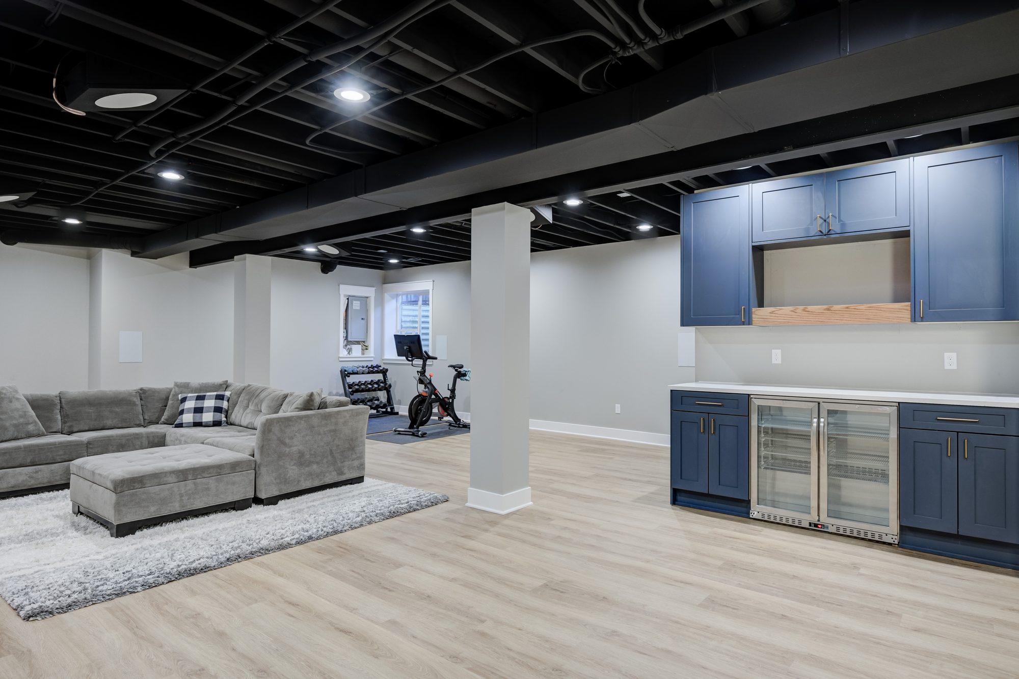 Open plan basement with a lounge, home gym and navy wet bar in a Royal Oak MI basement finishing project