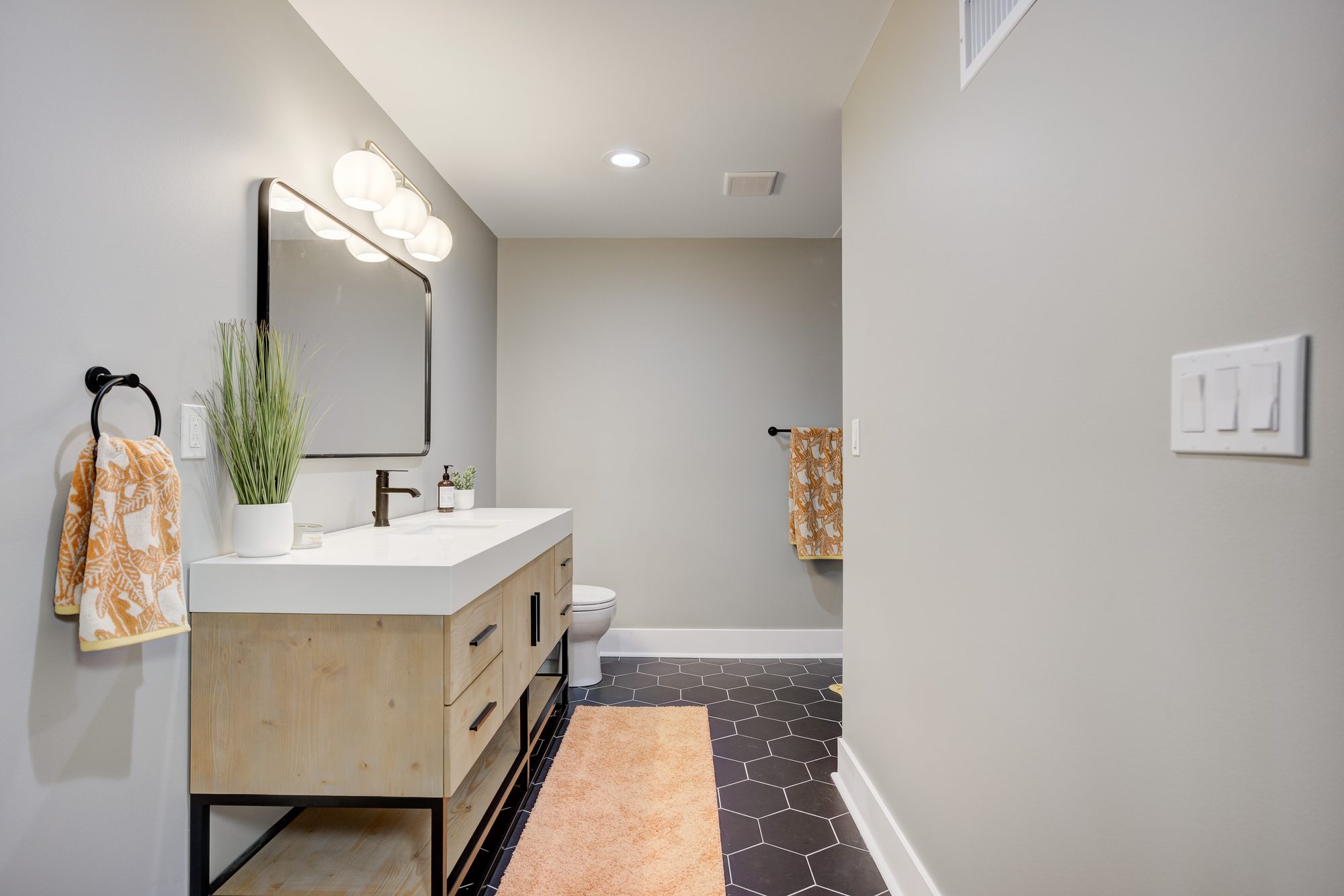 Basement bathroom with a light oak floating vanity, black fixtures and a black hexagon tile floor in Royal Oak MI