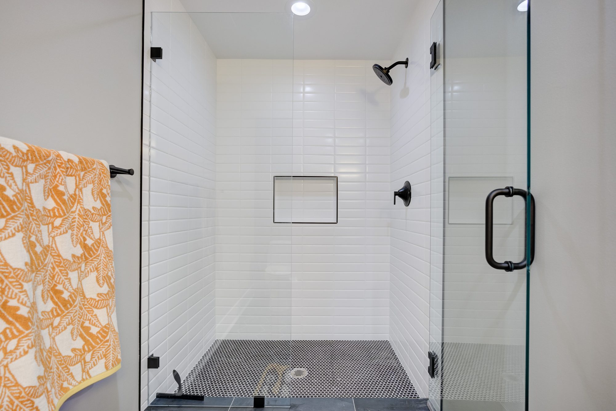 Walk in shower with white stacked tile, a penny tile floor and matte black fixtures in a Royal Oak MI basement bathroom