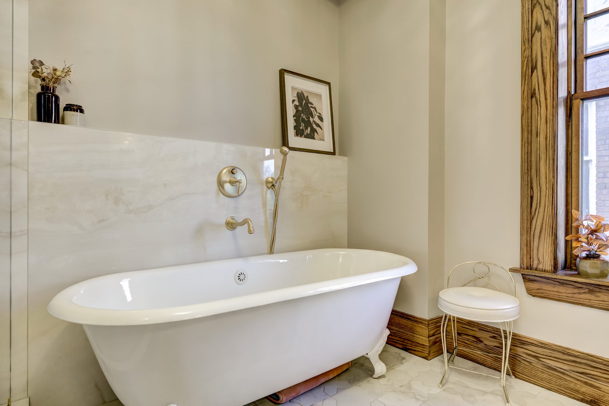Clawfoot soaking tub with a brushed brass tub filler and hand shower against slab marble in a Birmingham MI bathroom
