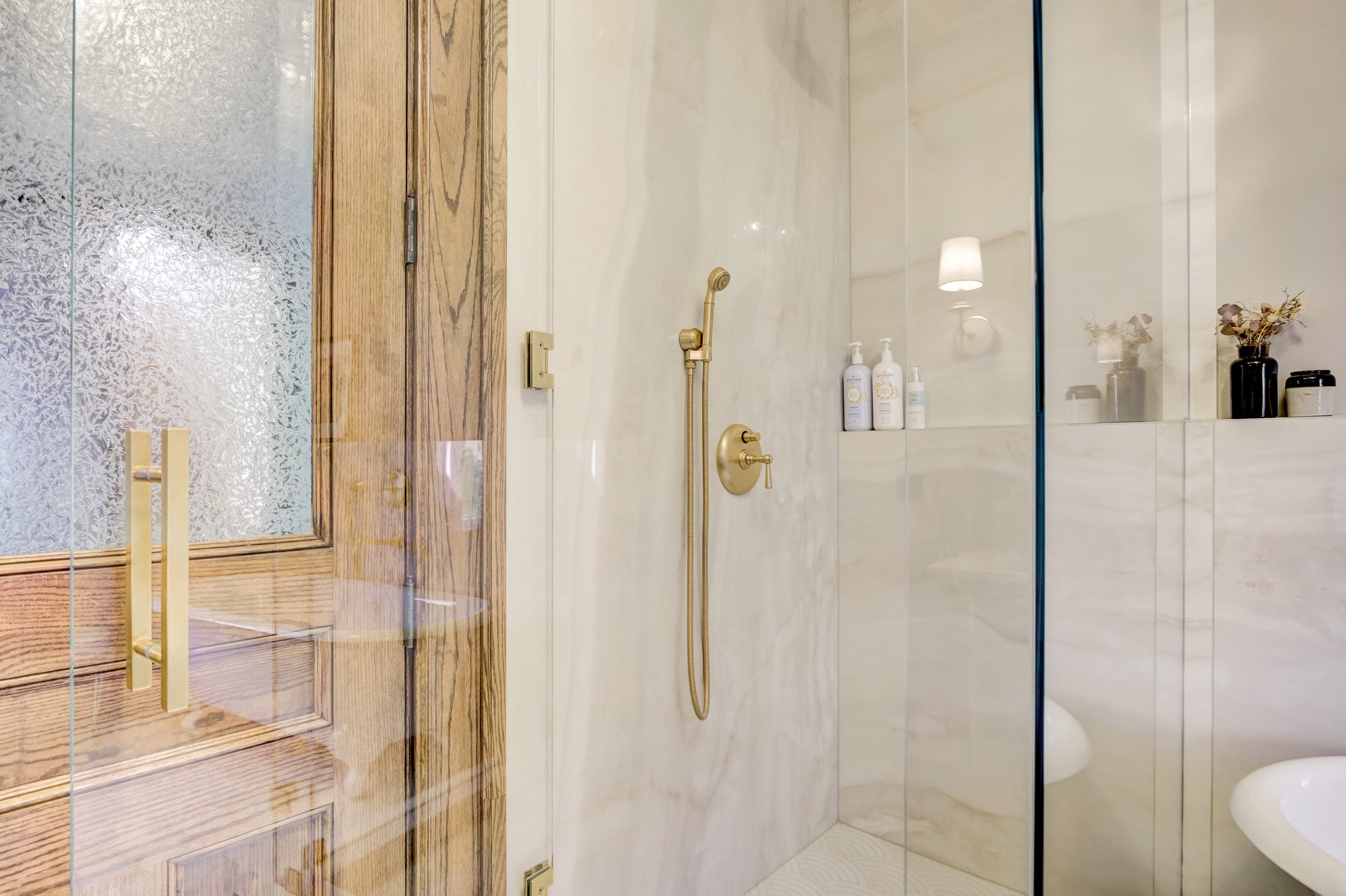 Frameless glass shower enclosure with brass fixtures and a built in niche shelf in a Birmingham MI bathroom