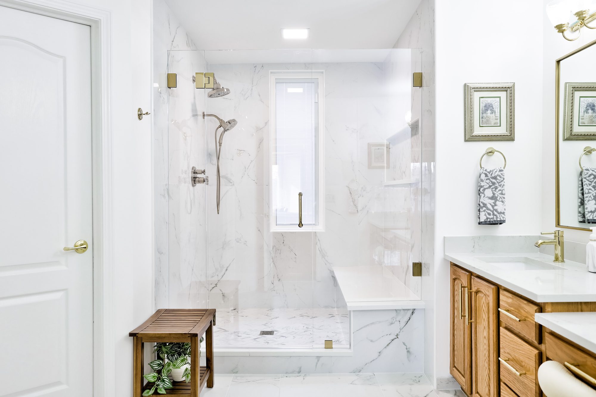 Remodeled bathroom in Birmingham MI with a marble look tile shower, quartz bench and oak vanity