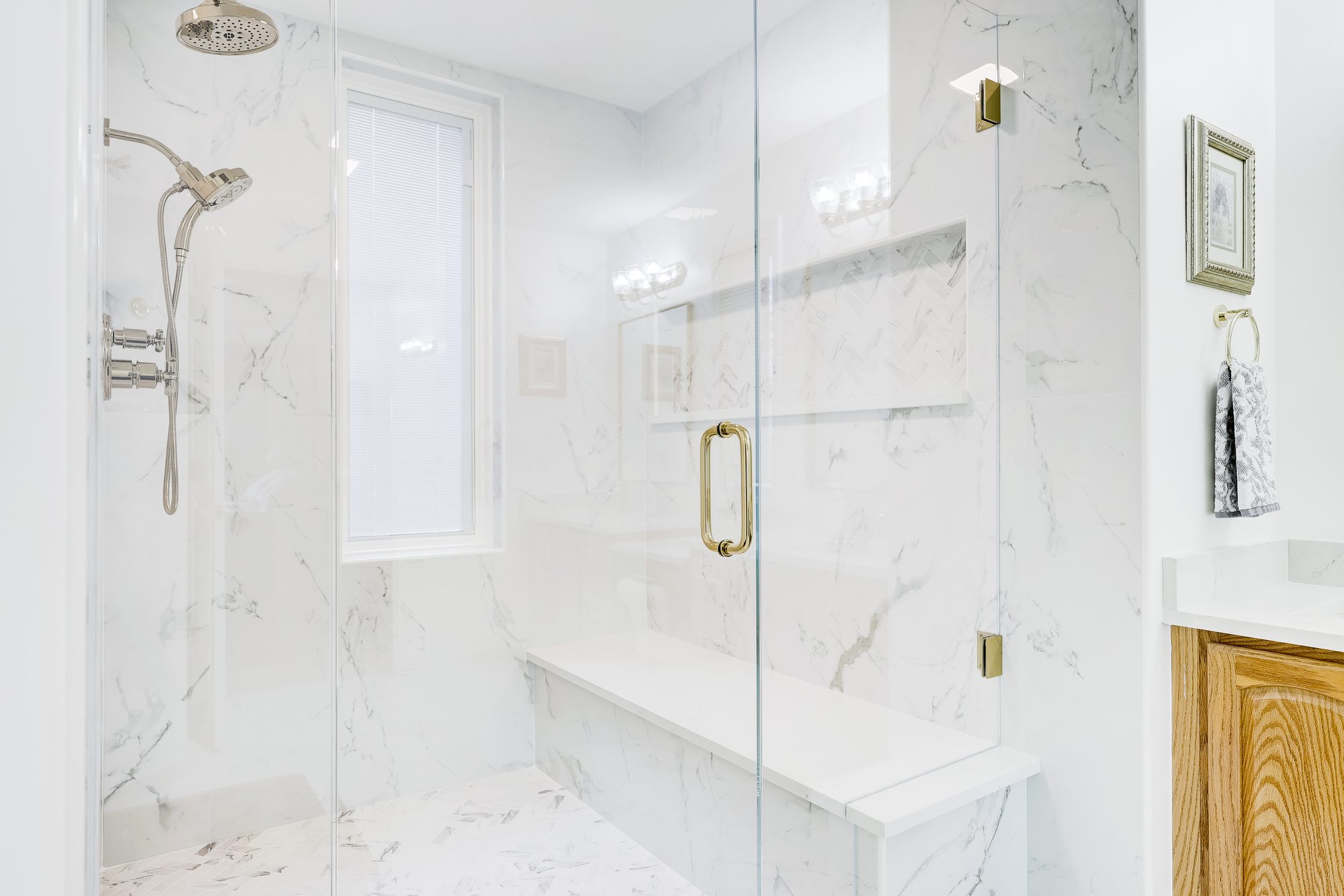 Walk in shower with a frameless glass door, full length quartz bench and herringbone tile niche in Birmingham MI