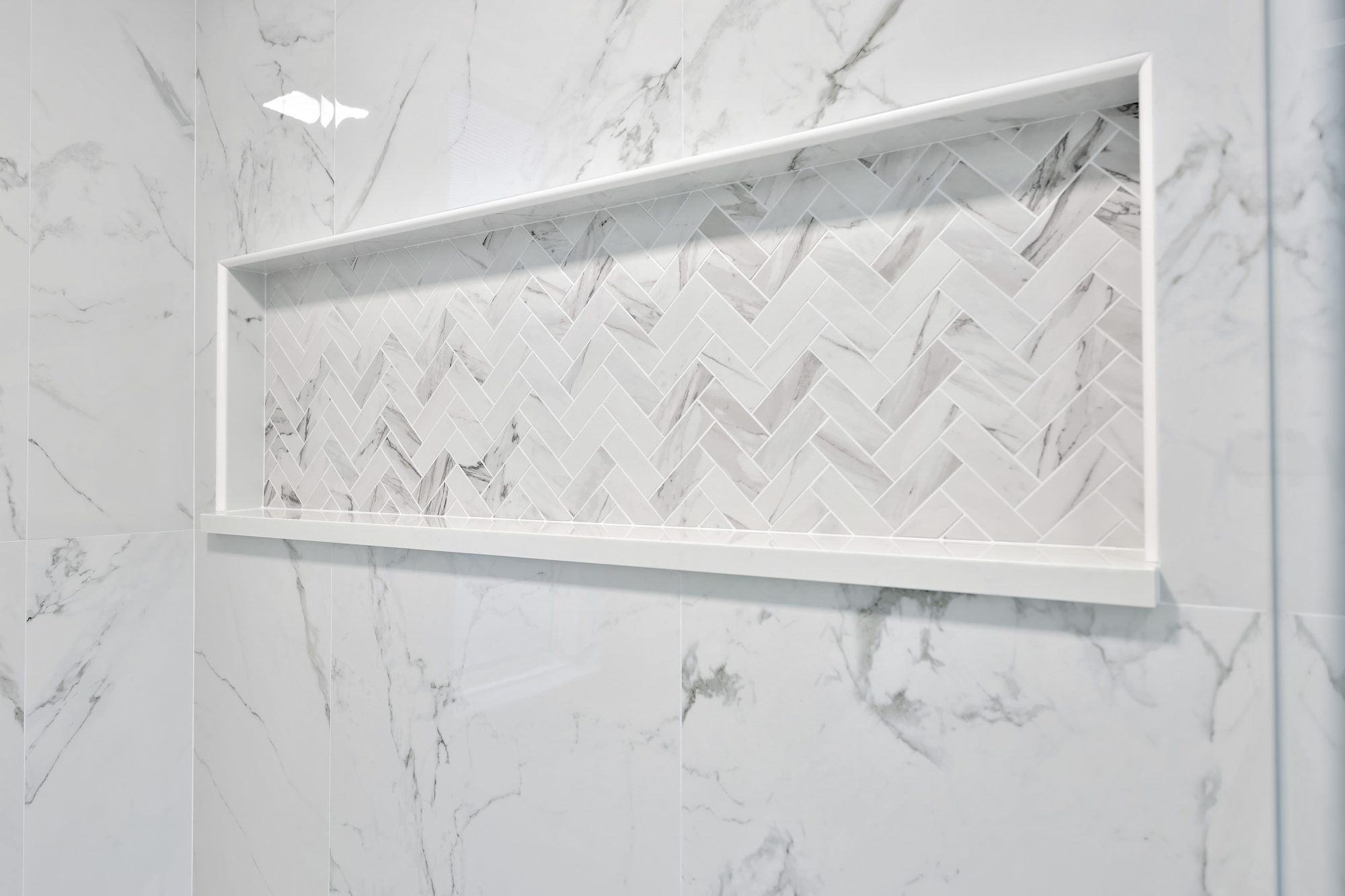 Full width shower niche in herringbone marble look tile with a quartz sill in a Birmingham MI bathroom