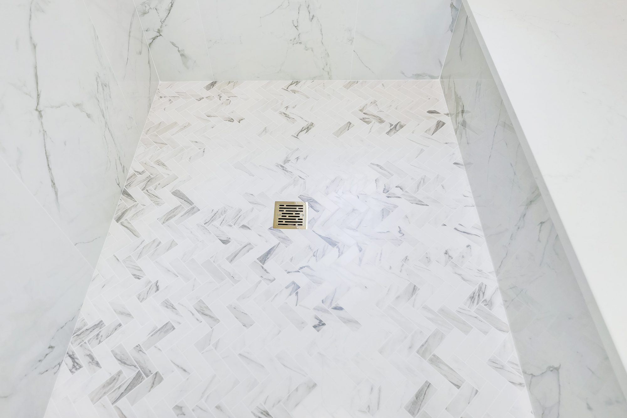 Herringbone marble look shower floor with a square brass drain in a Birmingham MI bathroom remodel