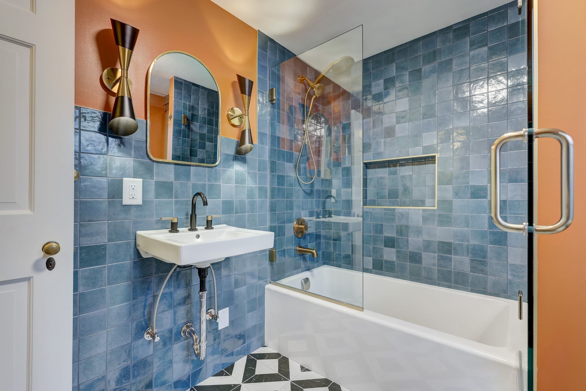 Wall mount sink and brass sconces looking toward the tiled tub in a Ferndale MI bathroom remodel