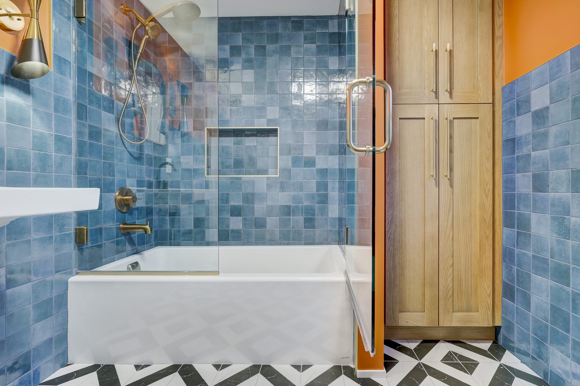 Alcove tub with a fixed glass panel beside a built in white oak linen tower in a Ferndale MI bathroom remodel
