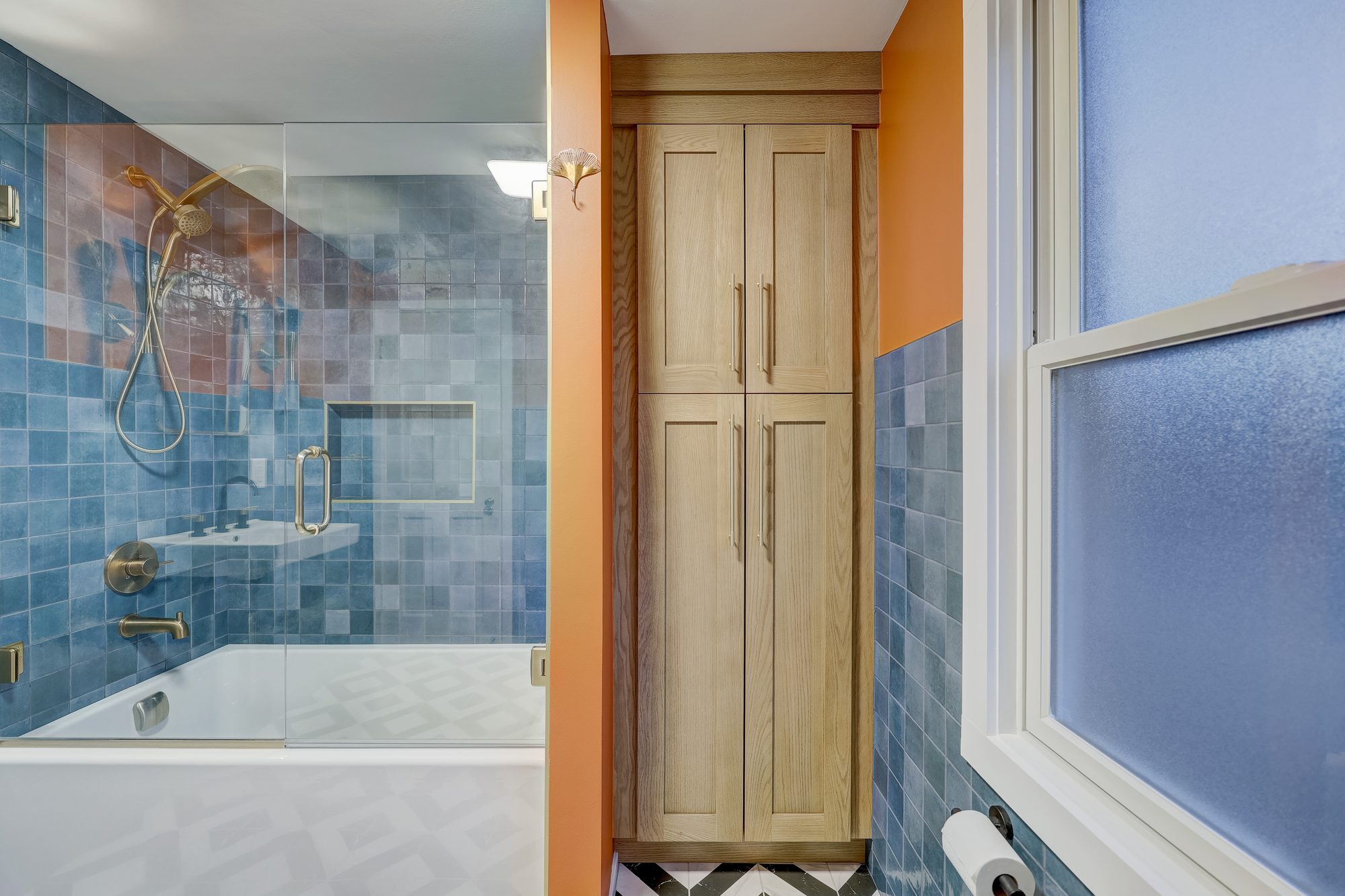 Built in white oak linen tower with a brass gingko sconce between the tub and the window in a Ferndale MI bathroom