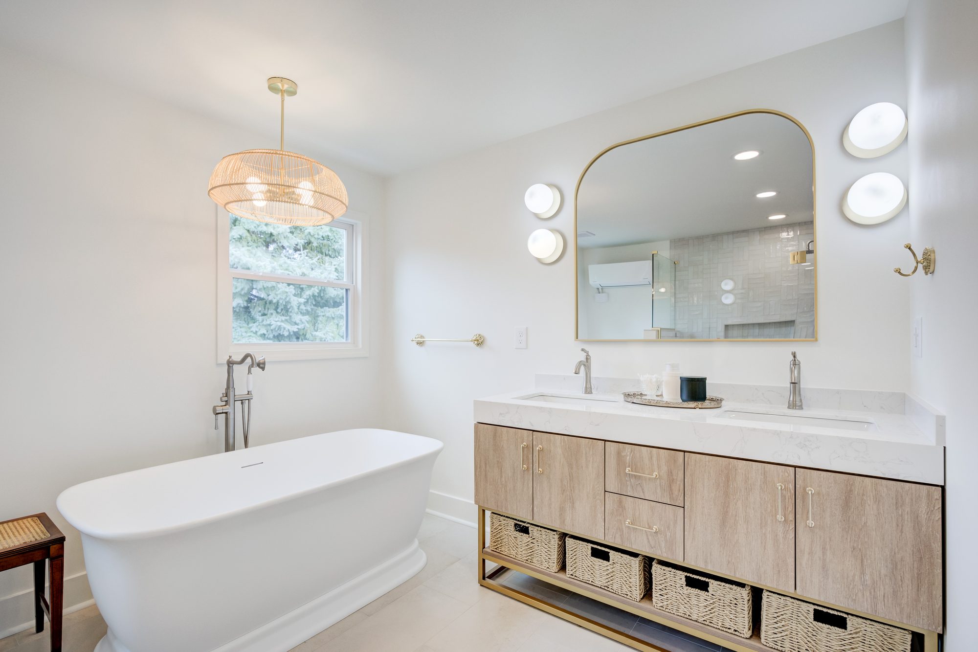 Light oak double vanity with a quartz counter, arched brass mirror and rattan chandelier in Huntington Woods MI