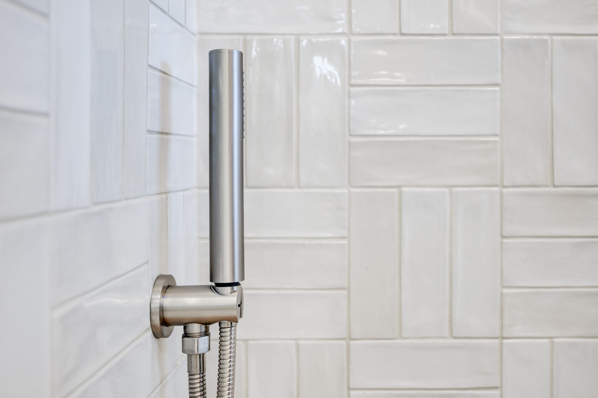 Hand shower on a wall mount against handmade white tile in a Huntington Woods MI bathroom remodel
