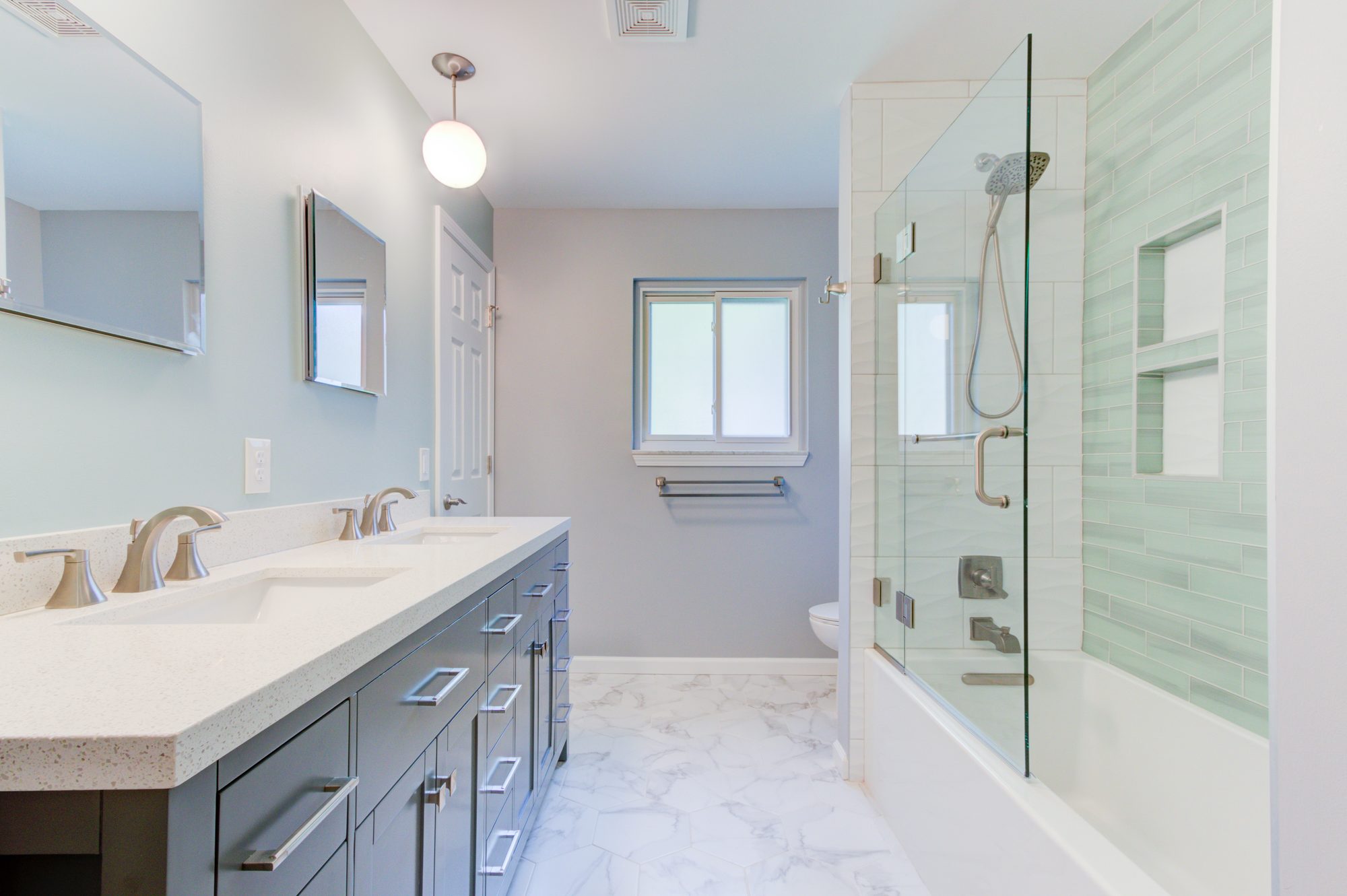 Remodeled bathroom in Troy MI with a double vanity, sea glass tile tub surround and marble look hexagon floor