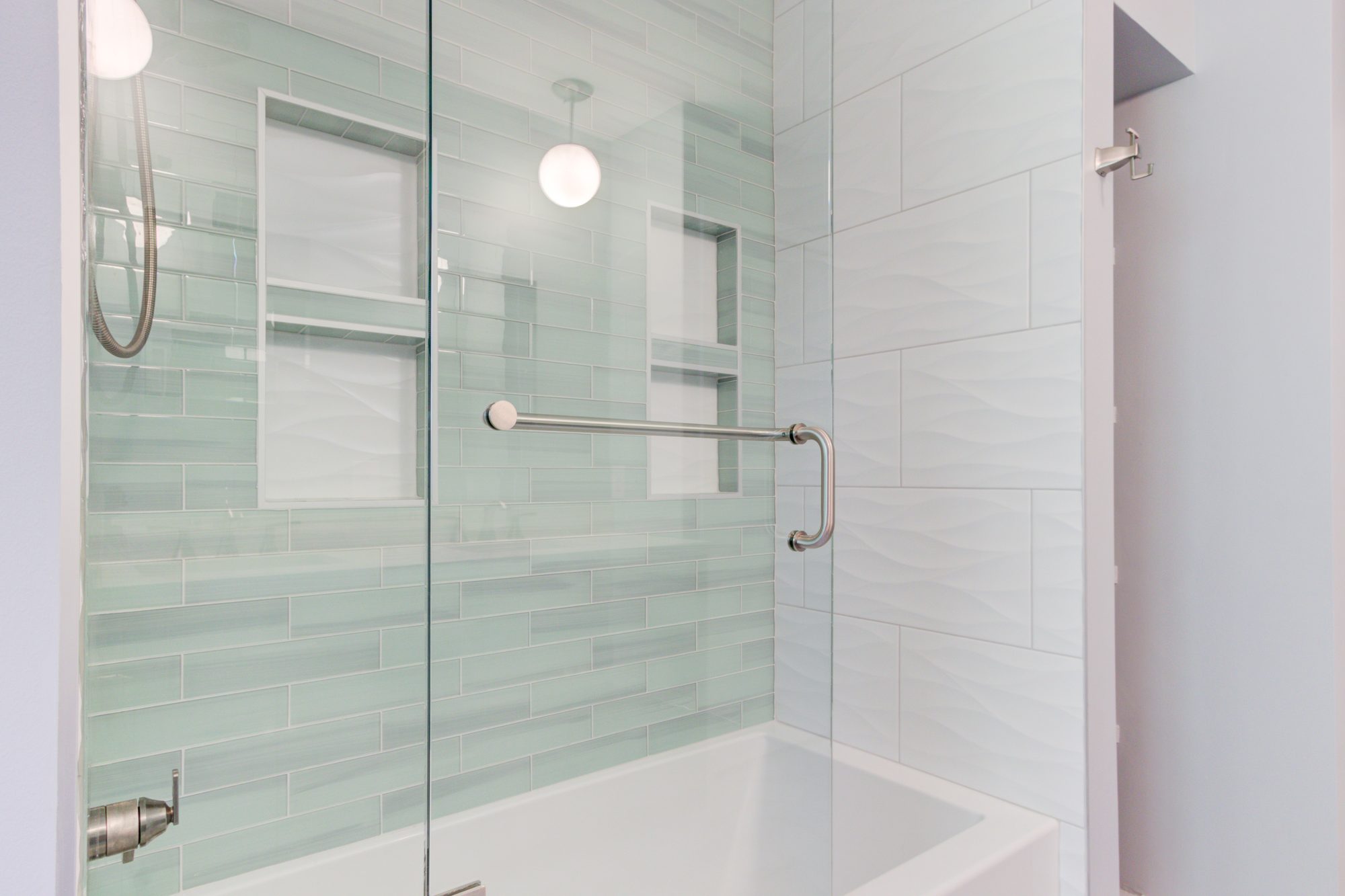 Tub and shower with a glass door, sea glass tile and textured white wall tile in a Troy MI bathroom remodel