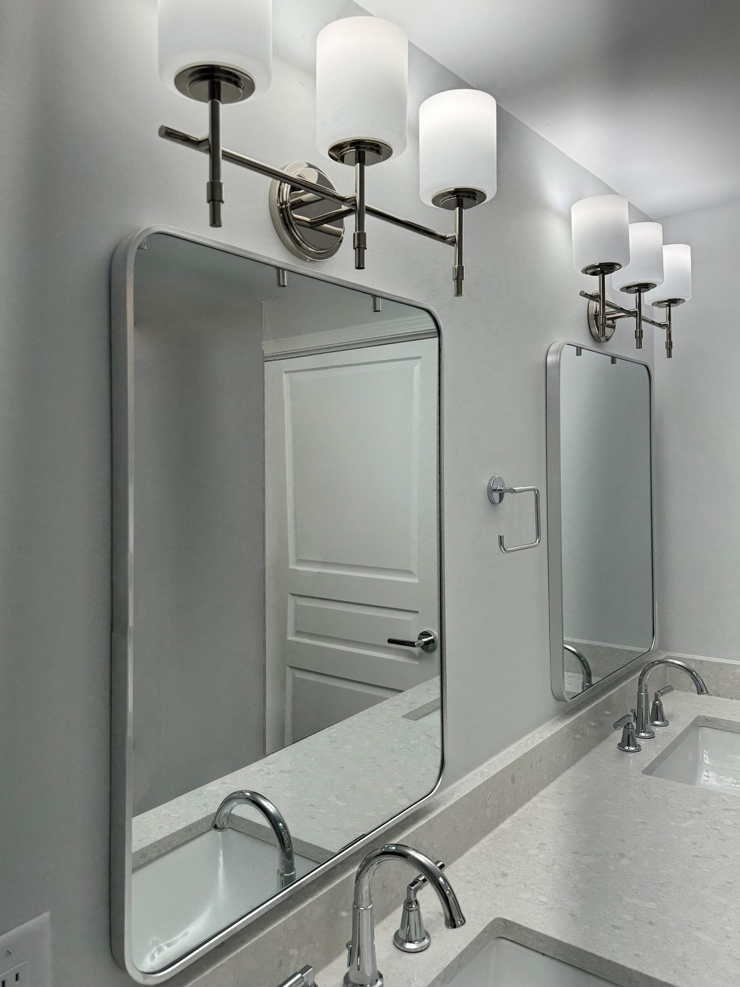 Rounded chrome framed mirrors and polished nickel sconces above a quartz vanity in a Troy MI bathroom