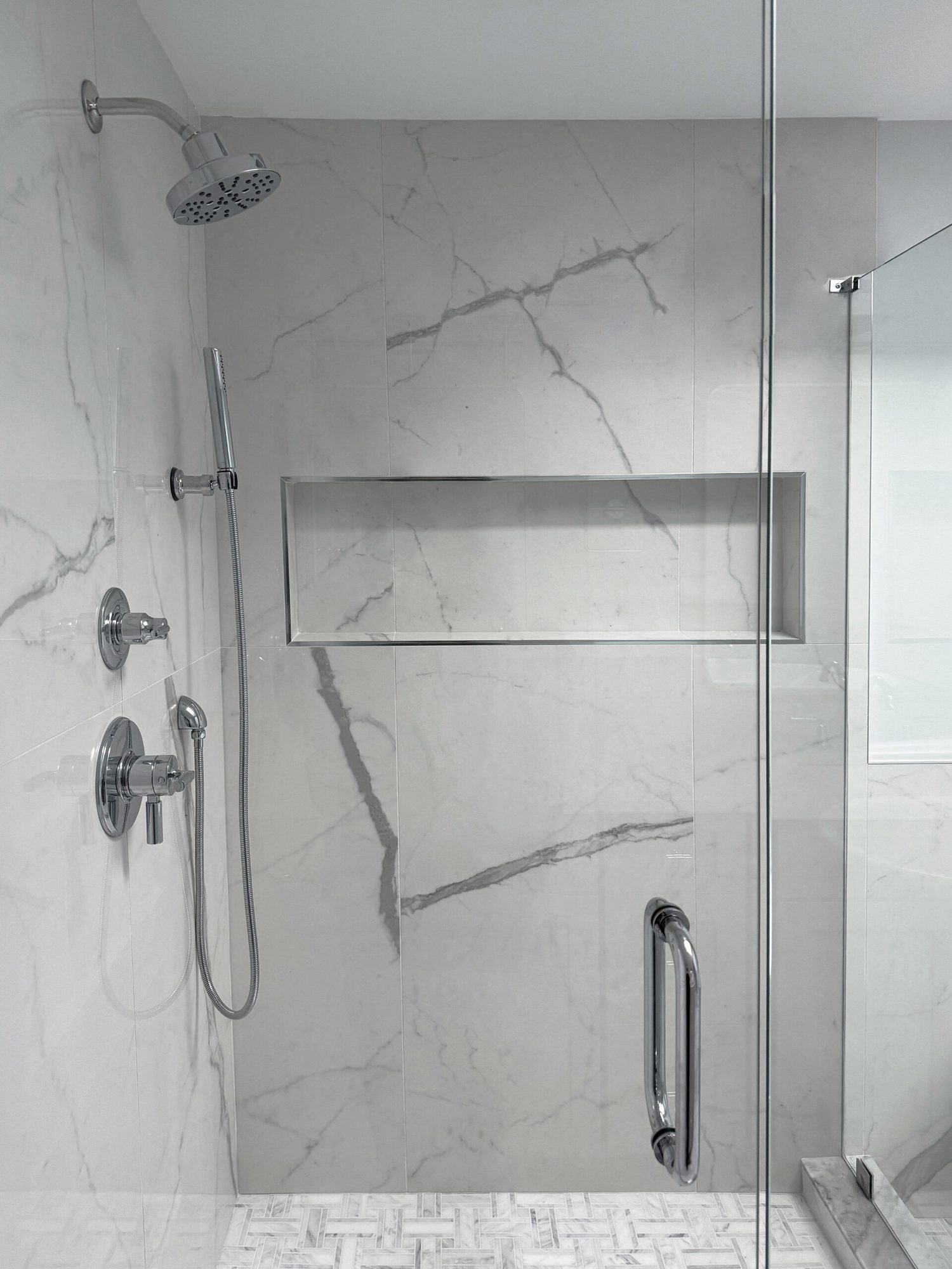 Shower interior with a rain head, hand shower and full width niche in marble look tile in a Troy MI bathroom