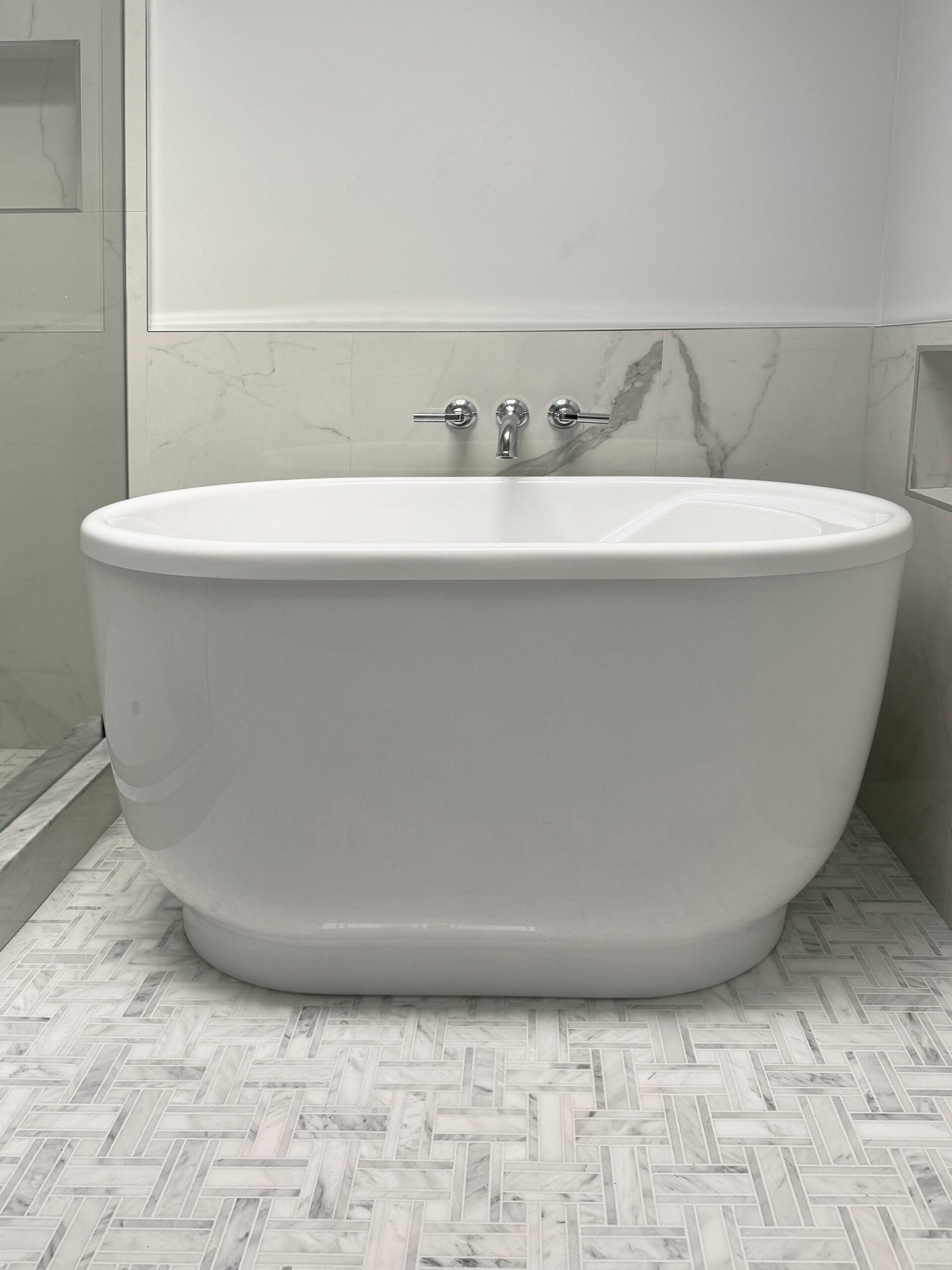 Freestanding soaking tub with a wall mount filler and marble look tile in a Troy MI bathroom remodel