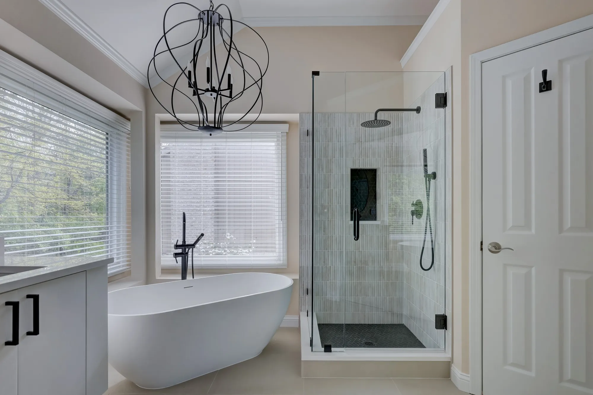 Soaking tub and glass shower below a black orb chandelier in a West Bloomfield MI bathroom remodel