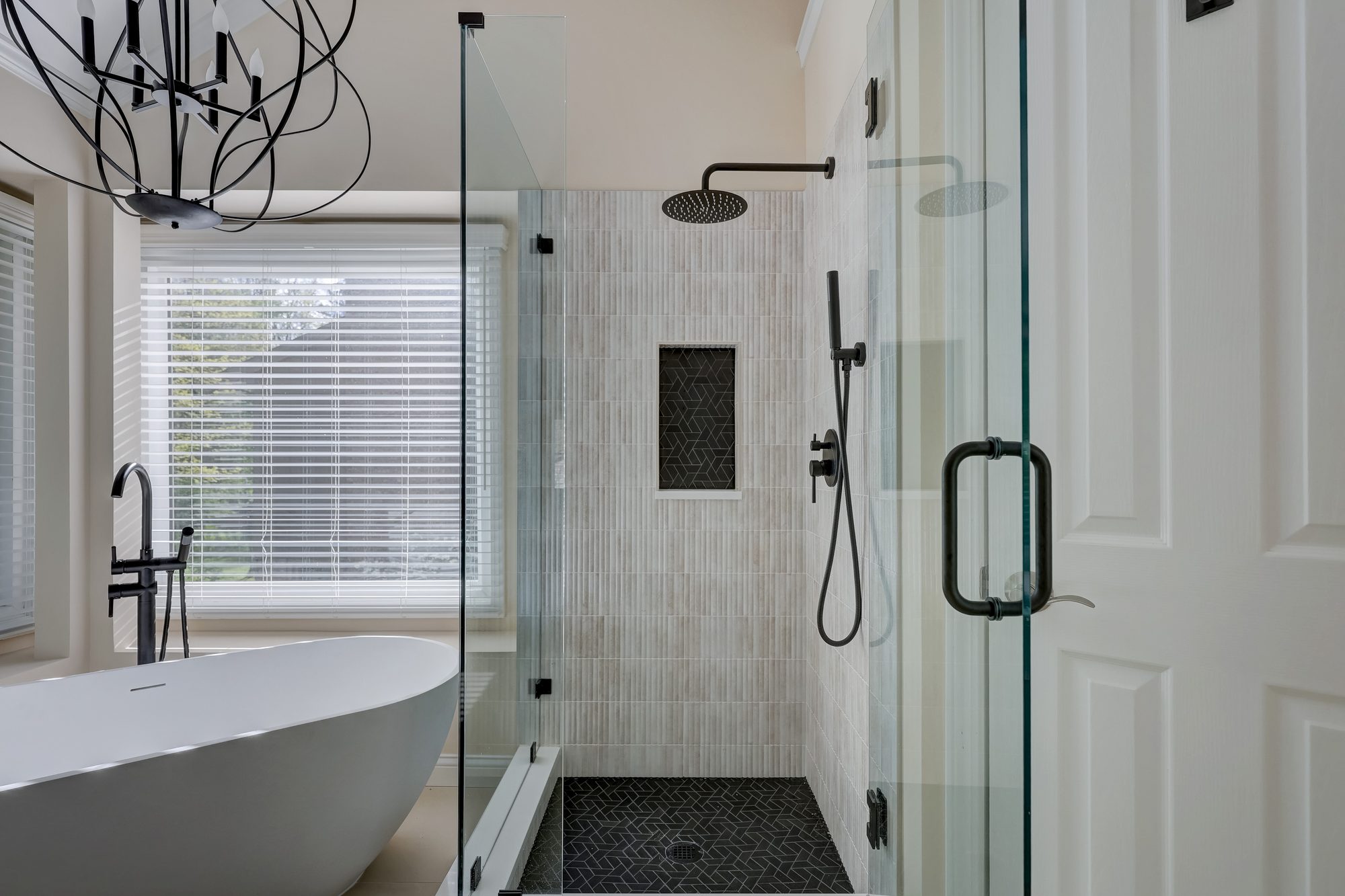 Glass shower with a matte black rain head, hand shower and black herringbone tile niche in a West Bloomfield MI bathroom