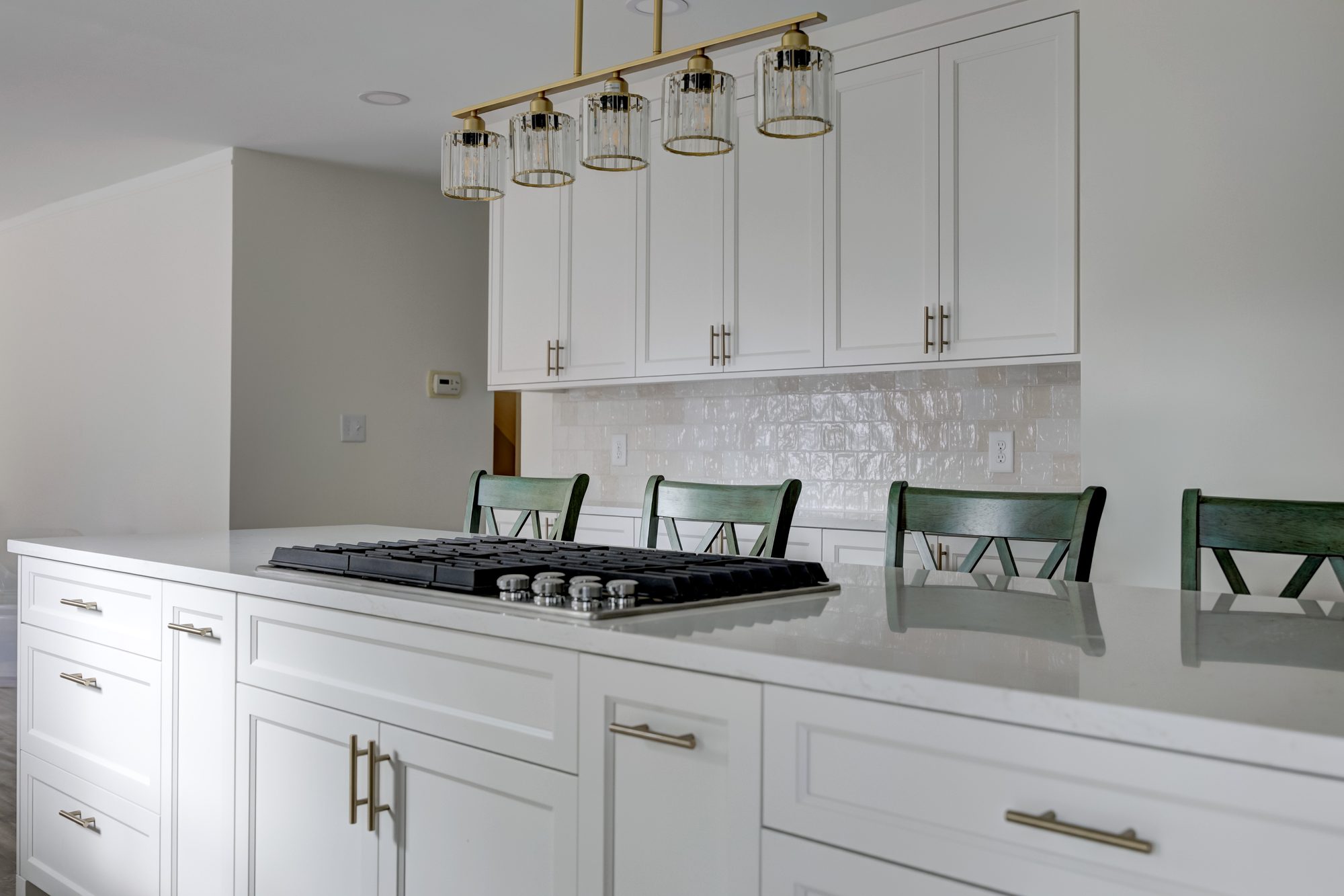 Gas cooktop set into the quartz island below a brass linear chandelier in a Beverly Hills MI kitchen remodel