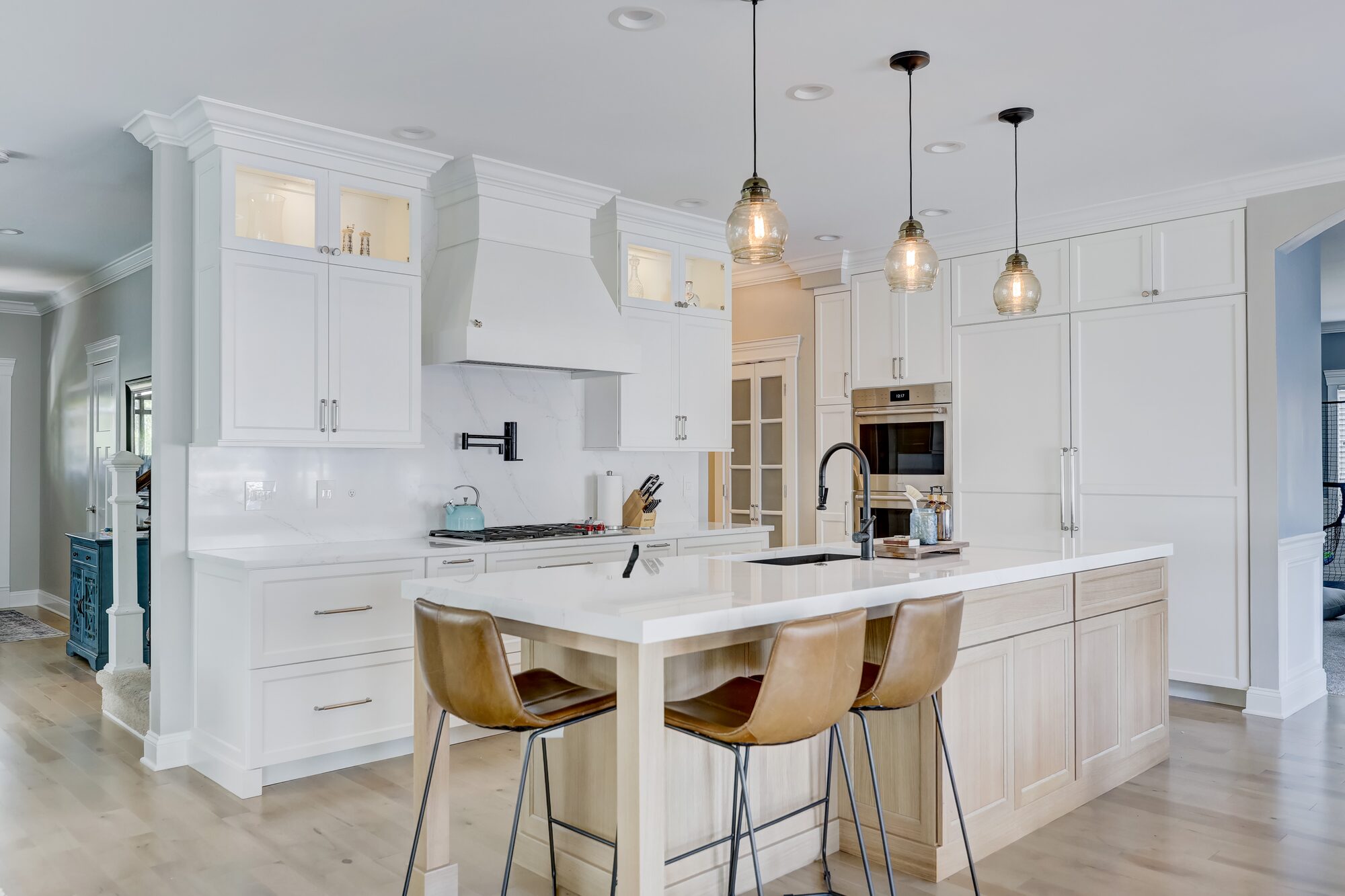 Custom painted range hood and white oak island with leather counter stools in a Birmingham MI kitchen remodel