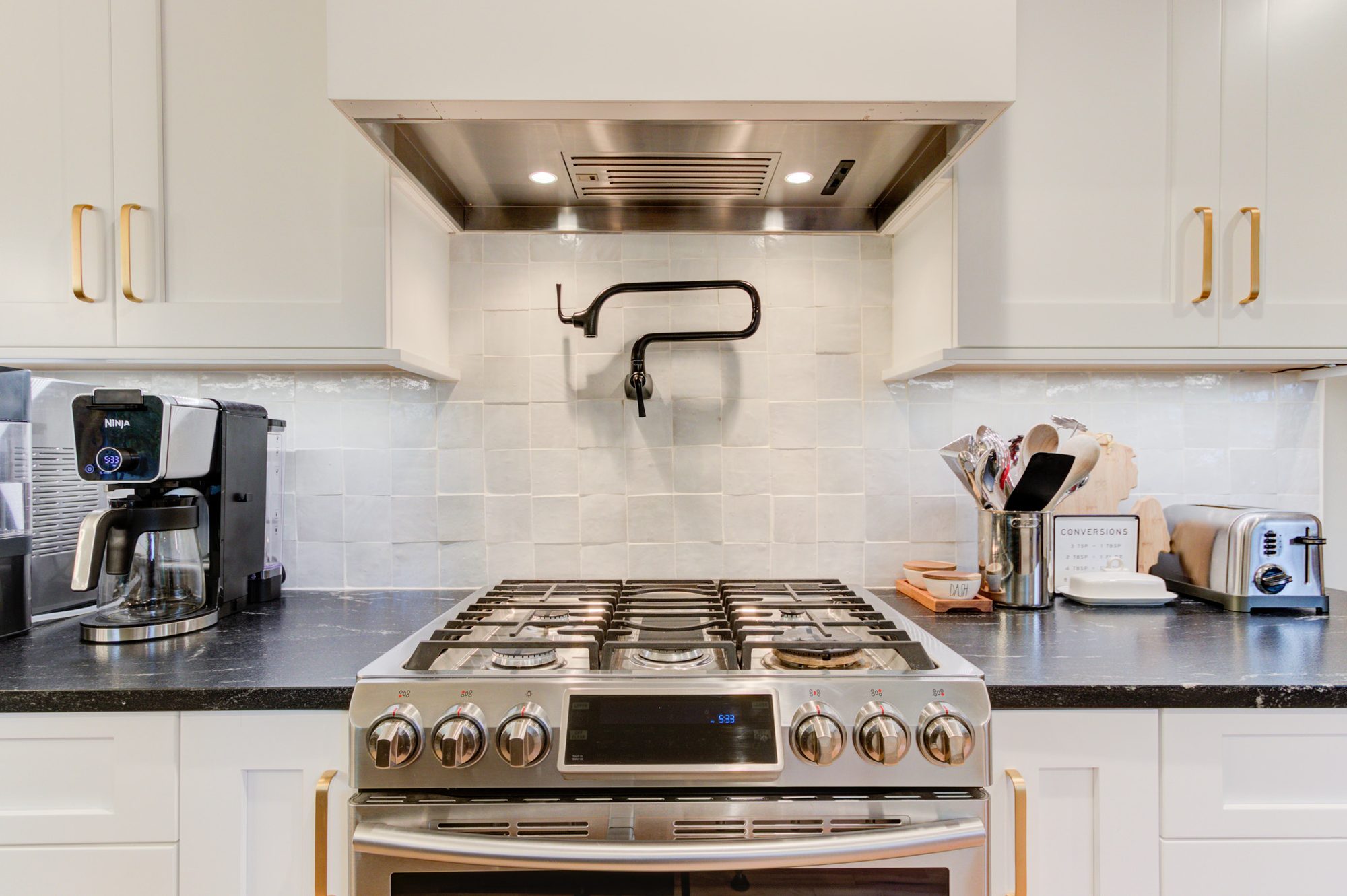 Gas range under a custom shiplap hood with a matte black pot filler and zellige tile in a Bloomfield Hills MI kitchen