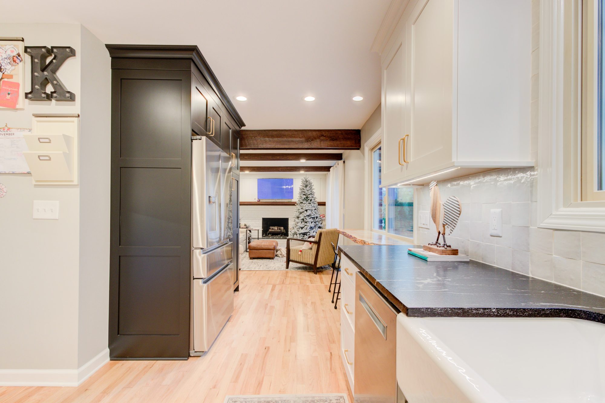 Kitchen looking past the charcoal pantry wall to the family room with exposed wood beams and a painted brick fireplace in a Bloomfield Hills MI remodel