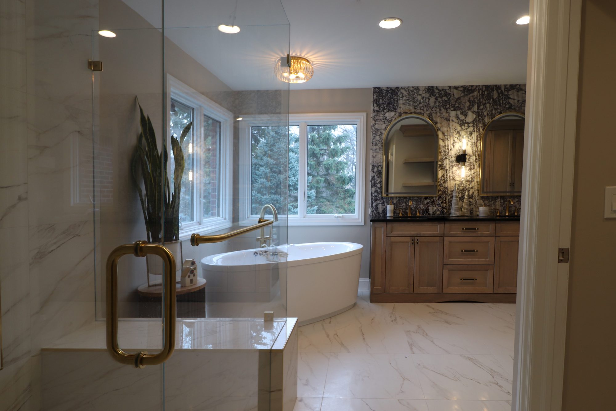 Remodeled master bathroom in Rochester Hills MI with a freestanding tub, marble look porcelain shower and brass fixtures