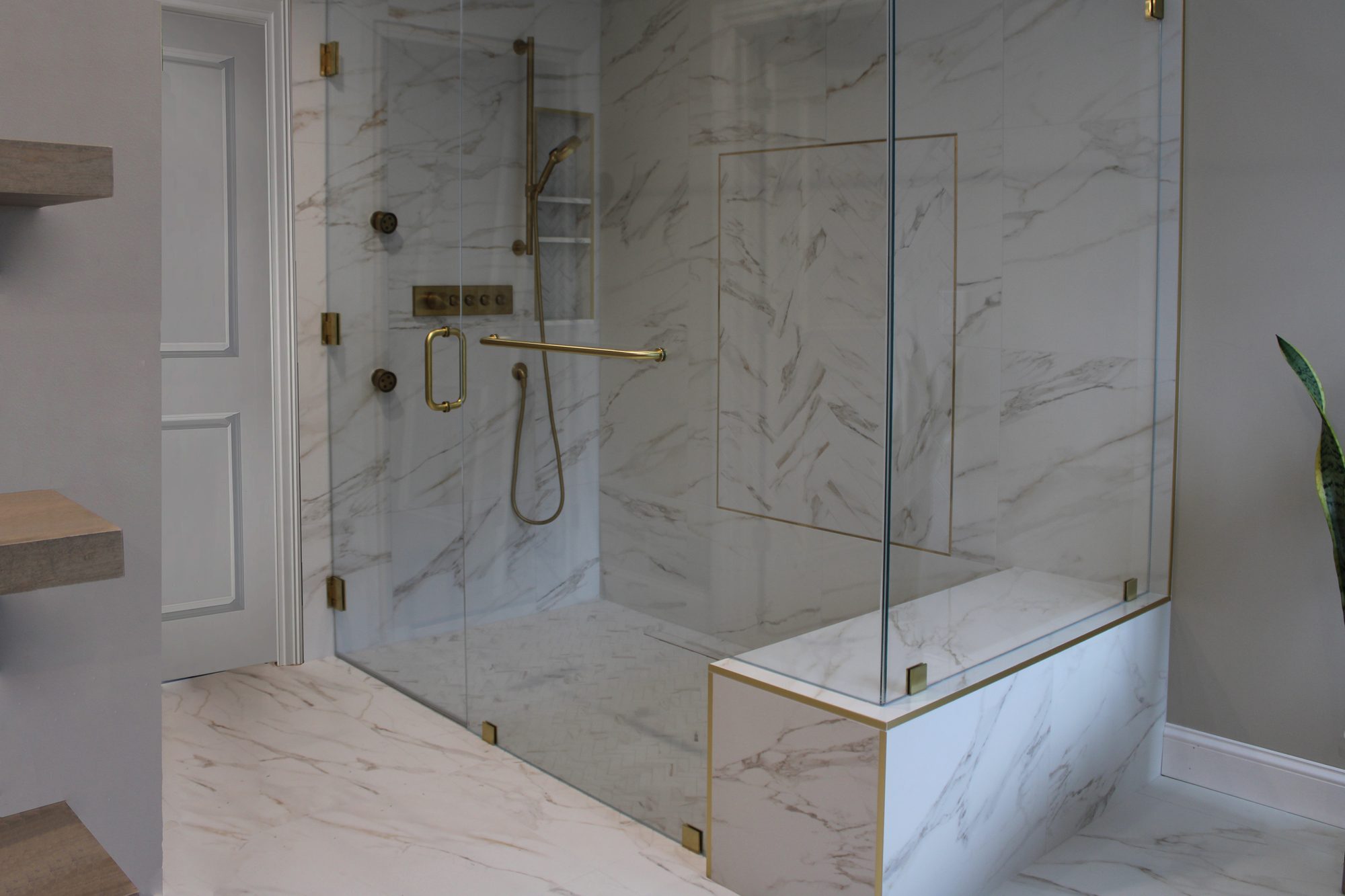 Frameless glass shower with a marble half wall, brass edge trim and built in bench in a Rochester Hills MI master bathroom