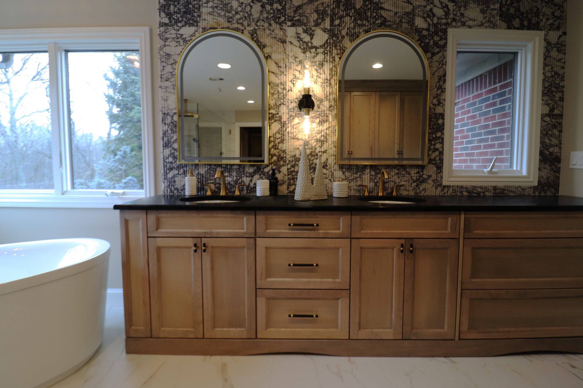 Double vanity with a fluted Calacatta Viola marble wall, black granite counter and arched brass mirrors in Rochester Hills MI