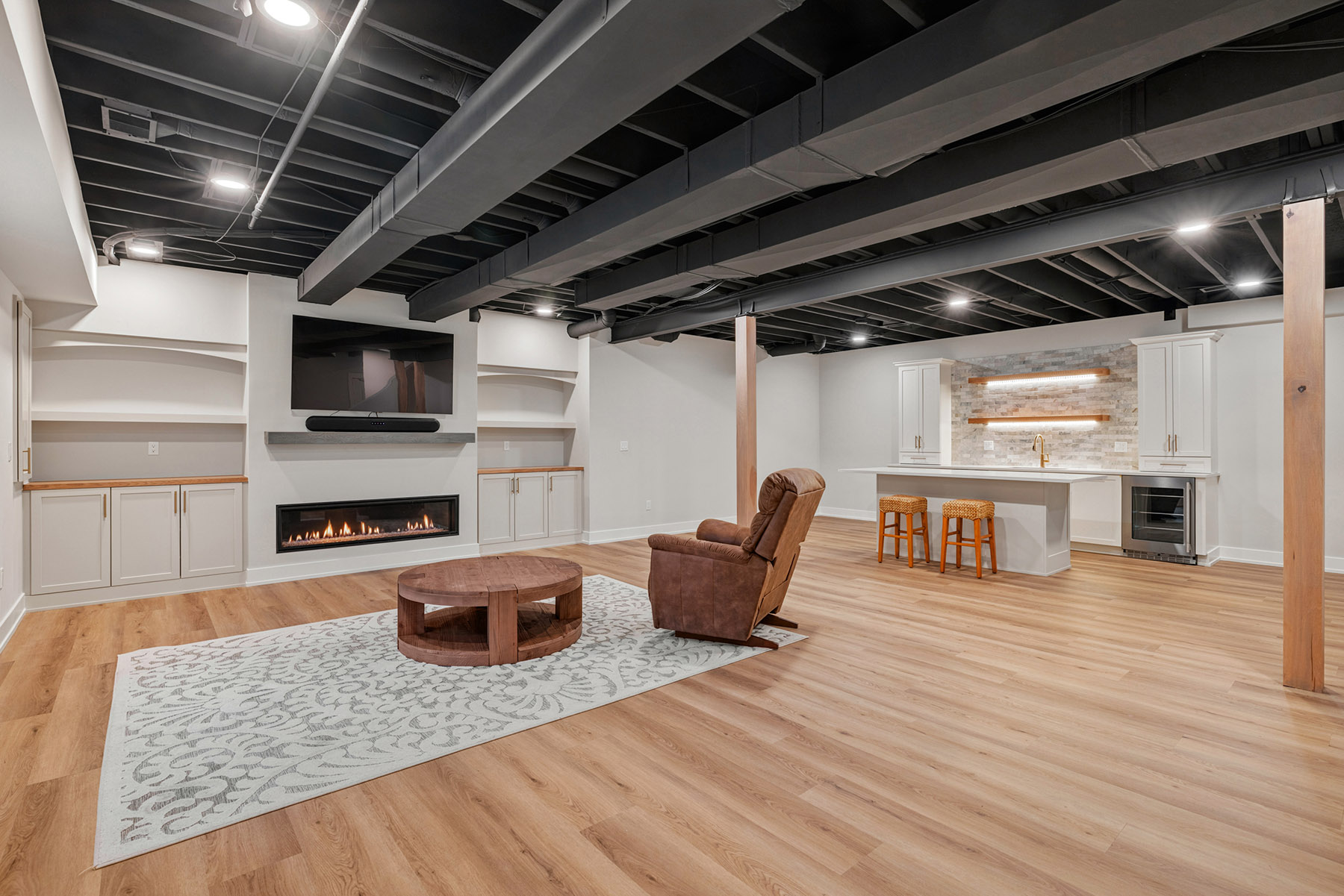 Finished basement in Birmingham MI with a linear gas fireplace, built in media wall and wet bar under a black exposed ceiling