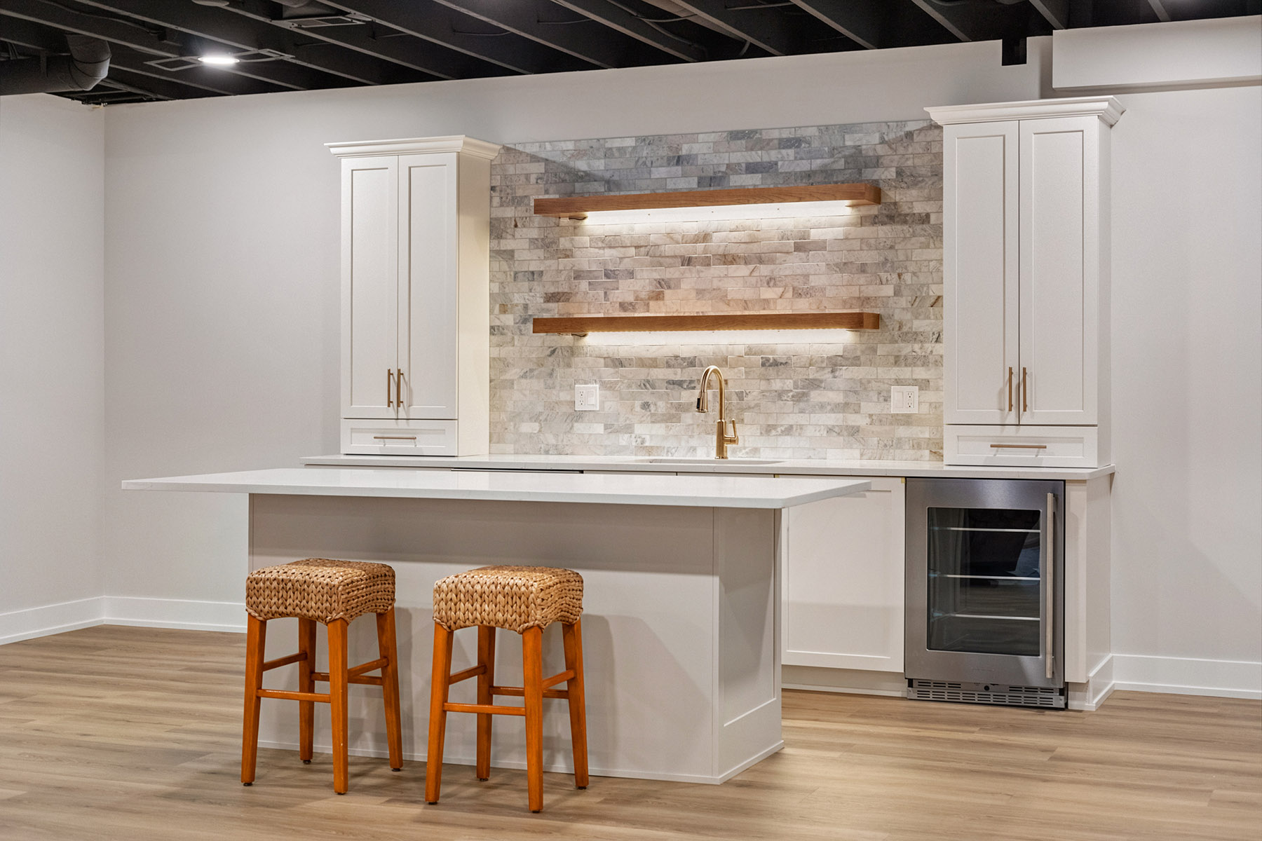Basement wet bar with quartz island, woven counter stools and beverage refrigerator in Birmingham MI