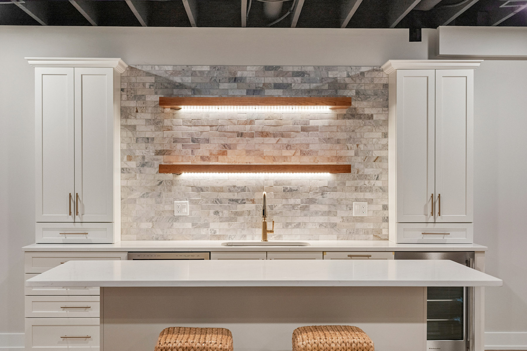 Wet bar wall with lit floating wood shelves over a textured tile backsplash between tall Dura Supreme cabinets