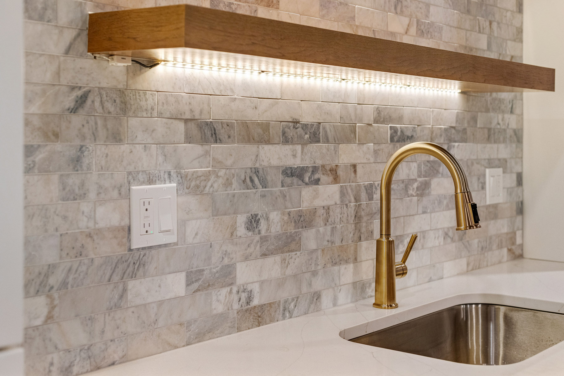 Brass bar faucet and undermount sink below lit floating shelves