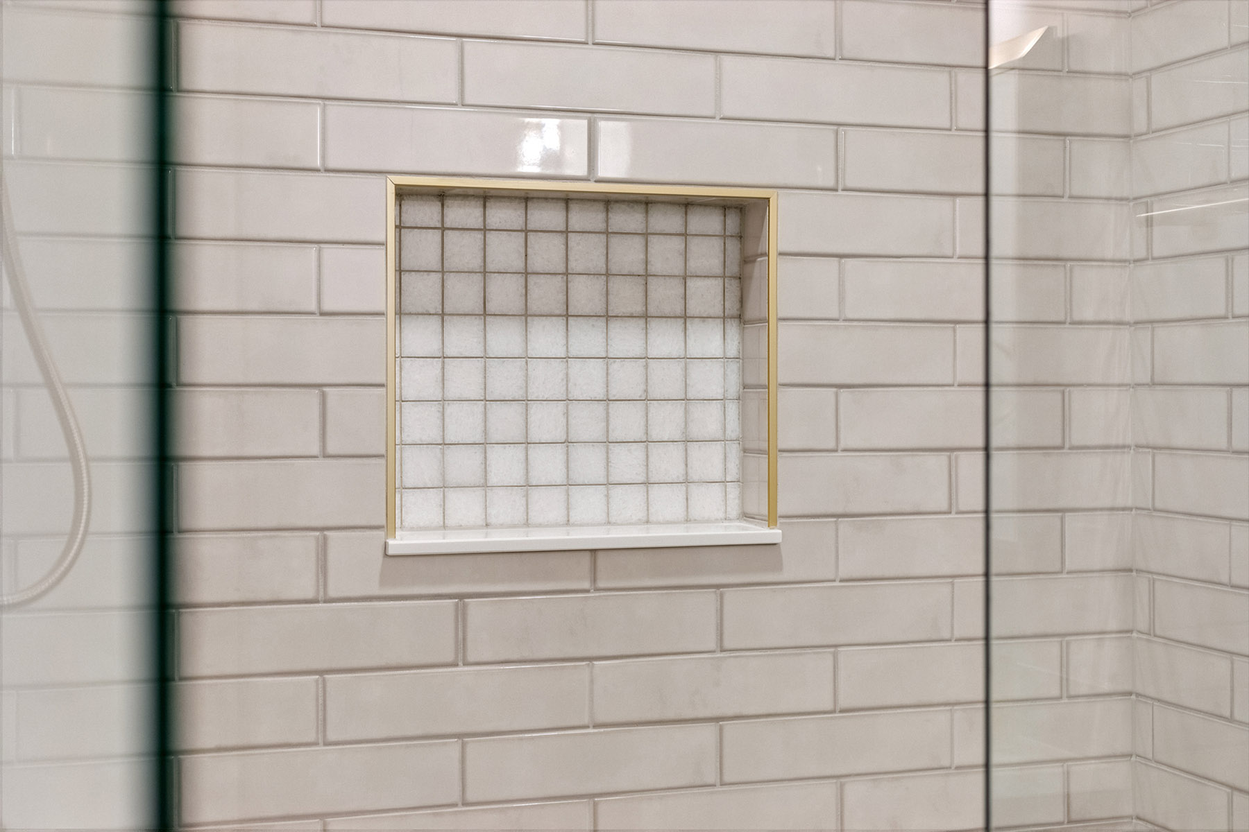 Recessed shower niche in white tile with brass trim